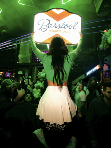 A Barstool Scottsdale event host holding the venue sign above the crowd